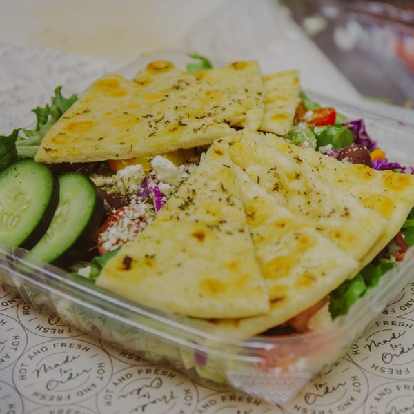 Mozillas Kitchen Mediterranean salad with cucumbers, feta, olives, and pita bread in a plastic container.