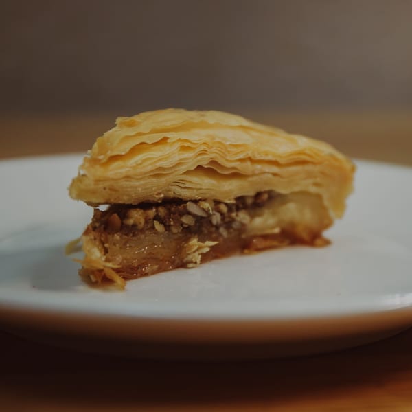 Close-up of a triangular piece of baklava with flaky pastry and a nutty, honeyed filling.