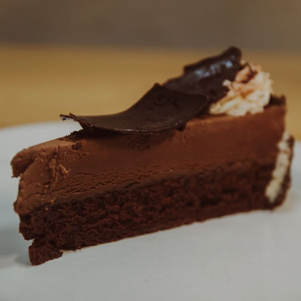A rich slice of chocolate cake with chocolate shavings and cream on a white plate.