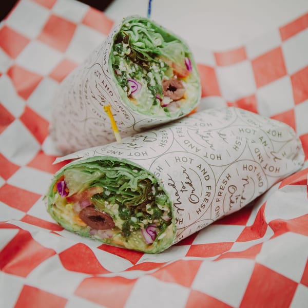 Two Mediterranean wraps, filled with fresh vegetables and olives, on red and white checkered paper.